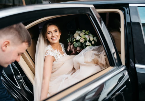 Bride in a white dress holding beautiful flowers sitting in a black luxury sedan